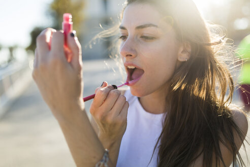 Porträt einer jungen Frau, die Lipgloss aufträgt - GIOF02318