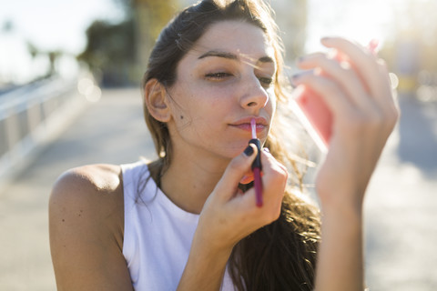 Porträt einer jungen Frau, die Lipgloss aufträgt, lizenzfreies Stockfoto