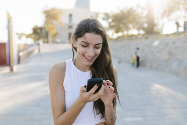 Portrait of smiling young woman looking at cell phone - GIOF02324