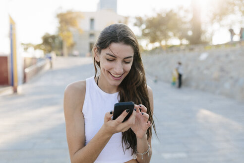 Porträt einer lächelnden jungen Frau, die auf ihr Mobiltelefon schaut - GIOF02324