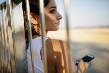 Smiling young woman leaning against railing at sunset - GIOF02327