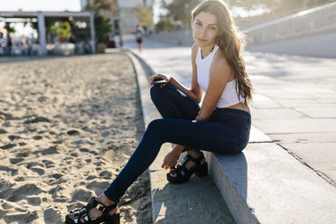 Porträt einer jungen Frau, die bei Sonnenuntergang auf der Strandpromenade sitzt - GIOF02328