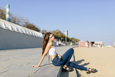 Junge Frau entspannt sich auf der Strandpromenade bei Sonnenuntergang - GIOF02330