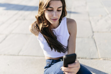 Young woman relaxing on beach promenade looking at cell phone - GIOF02333