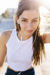 Porträt einer lächelnden jungen Frau mit Kopfhörern bei Sonnenuntergang - GIOF02336