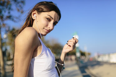 Junge Frau entspannt sich auf der Strandpromenade bei Sonnenuntergang und hört Musik mit Kopfhörern - GIOF02338
