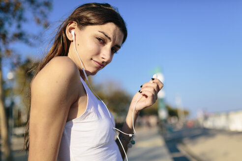 Junge Frau entspannt sich auf der Strandpromenade bei Sonnenuntergang und hört Musik mit Kopfhörern - GIOF02338