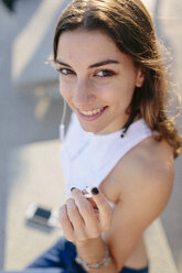 Portait of smiling young woman listening music with earphones at sunset - GIOF02339