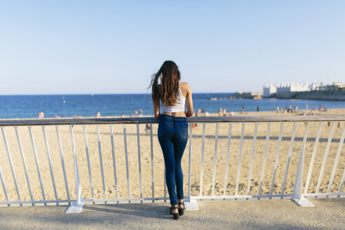 Rückenansicht einer jungen Frau, die an der Strandpromenade steht und auf das Meer blickt - GIOF02341