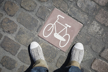 Person standing next to pictogram with bicycle on cobblestone pavement - RORF00677