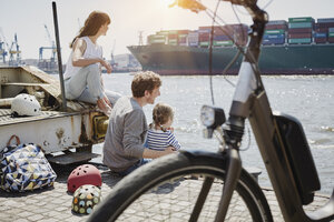 Deutschland, Hamburg, Familie macht eine Pause von einer Fahrradtour an der Elbe und beobachtet ein Containerschiff - RORF00684