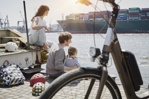 Deutschland, Hamburg, Familie macht eine Pause von einer Fahrradtour an der Elbe und beobachtet ein Containerschiff - RORF00684
