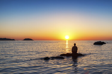 Spanien, Menorca, Playa de Cavalleria, Mann auf Felsen im Meer bei Sonnenuntergang - SMAF00725