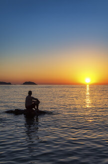 Spanien, Menorca, Playa de Cavalleria, Mann auf Felsen im Meer bei Sonnenuntergang - SMAF00726