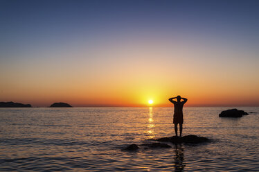Spanien, Menorca, Playa de Cavalleria, Mann auf Felsen im Meer bei Sonnenuntergang - SMAF00727