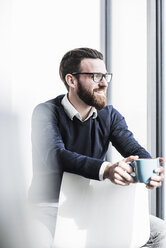 Young businessman sitting on chair drinking coffee - UUF10146