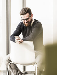 Young businessman sitting on chair using smart phone - UUF10147