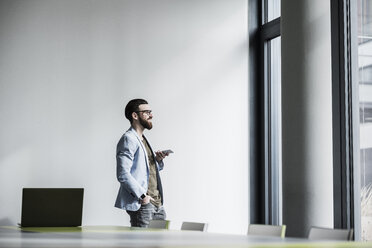 Young businessman standing in office, using smart phone - UUF10148