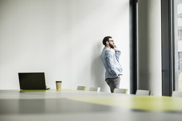 Junger Geschäftsmann steht im Büro und benutzt sein Smartphone - UUF10149