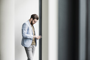 Junger Geschäftsmann steht im Büro und benutzt sein Smartphone - UUF10150