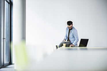 Young businessman sitting on desk, working - UUF10158