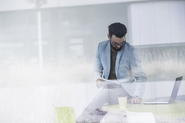 Young businessman sitting on desk, working - UUF10159