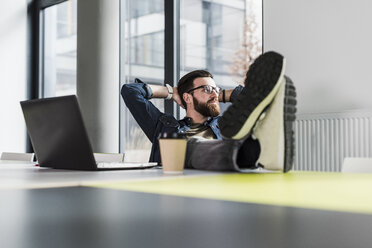 Young casual businessman sitting in office with feet up and a cup of coffee - UUF10162