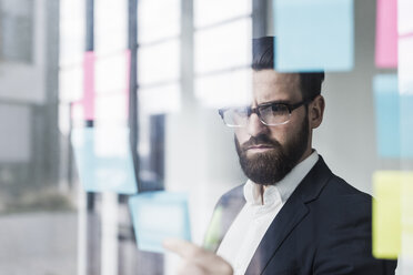 Young businessman attaching adhesive notes to glass pane - UUF10169