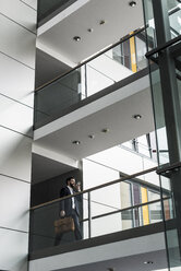 Businessman walking in office building, while using smart phone - UUF10186