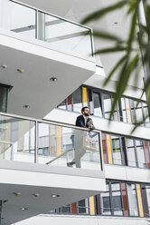 Businessman standing on landing of an office building, talking on the phone - UUF10187