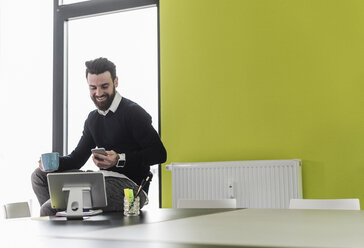 Junger Geschäftsmann sitzt im Büro und benutzt mobile Geräte - UUF10202