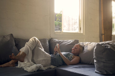 Smiling woman lying on the couch using cell phone - KNTF00816