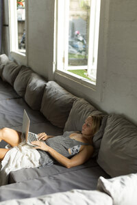 Blonde Frau auf der Couch liegend mit Laptop - KNTF00820