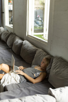 Blond woman lying on the couch using laptop - KNTF00820