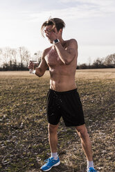 Sportler mit nacktem Oberkörper in ländlicher Landschaft, der sich Wasser über sein Gesicht gießt - UUF10214