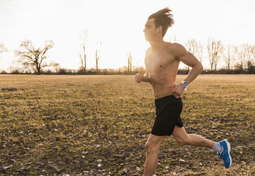 Barechested man running in rural landscape - UUF10216