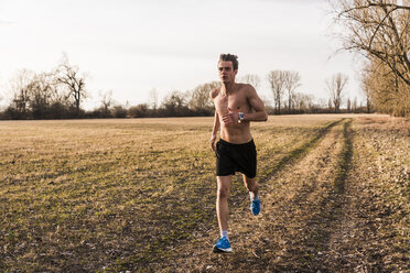 Barechested man running in rural landscape - UUF10217