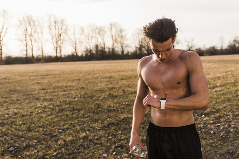 Barechested athlete in rural landscape looking on smartwatch stock photo
