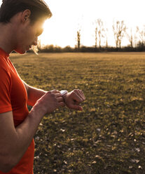 Sportler in ländlicher Landschaft mit Blick auf die Smartwatch - UUF10224