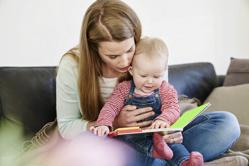 Mutter und kleines Mädchen zu Hause beim Betrachten eines Buches - FMKF03582