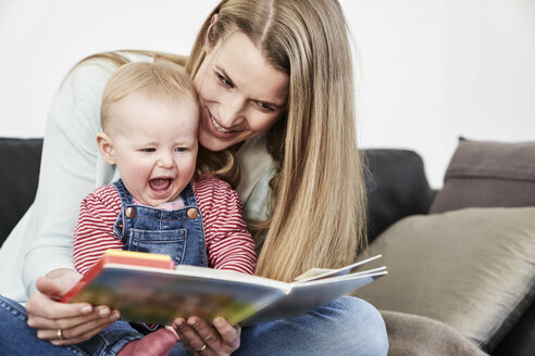 Mutter und glückliches kleines Mädchen zu Hause beim Betrachten eines Buches - FMKF03583
