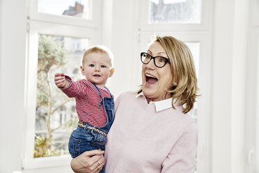 Happy grandmother carrying baby girl at home - FMKF03584