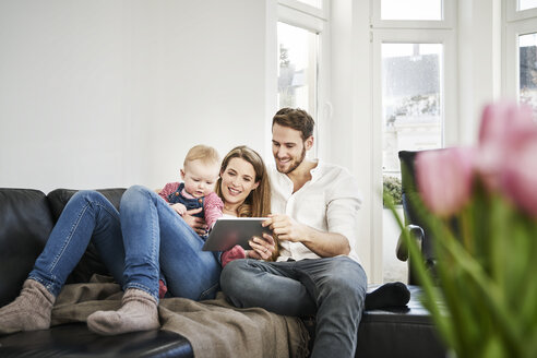 Eltern mit Baby Mädchen Blick auf Tablet auf Couch - FMKF03590