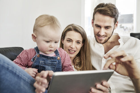 Eltern mit Baby Mädchen Blick auf Tablet auf Couch - FMKF03592