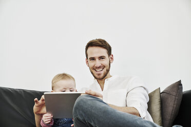 Father with baby girl using tablet on couch - FMKF03594