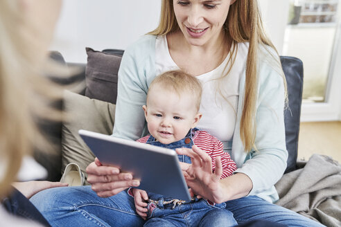 Mutter und kleines Mädchen zu Hause mit Blick auf das Tablet - FMKF03595