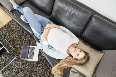 Woman at home lying on couch next to laptop - FMKF03616