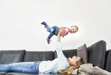 Happy mother lifting up baby girl on couch - FMKF03619