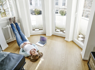 Woman at home lying on the floor next to laptop - FMKF03626