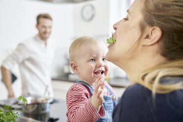 Mother with baby girl in kitchen eating herbs - FMKF03643